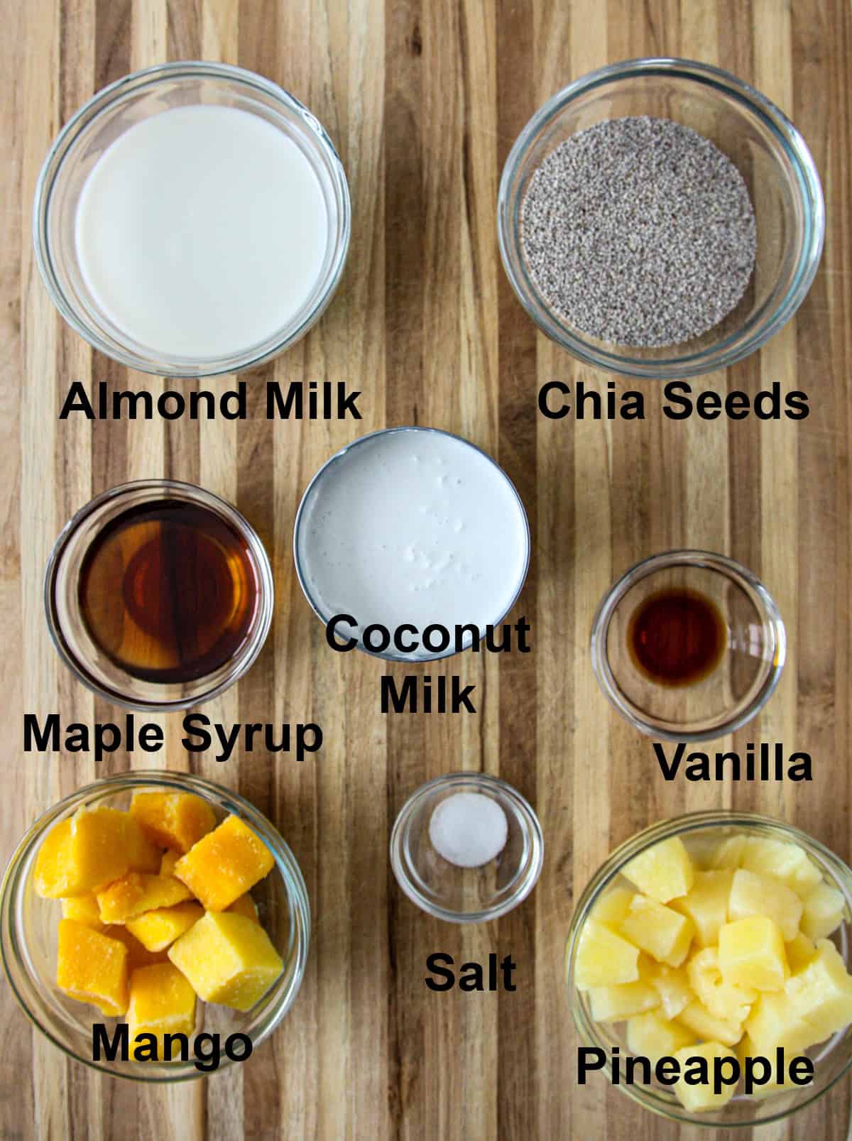 All of the ingredients for coconut milk chia pudding in glass bowls on a wooden board.