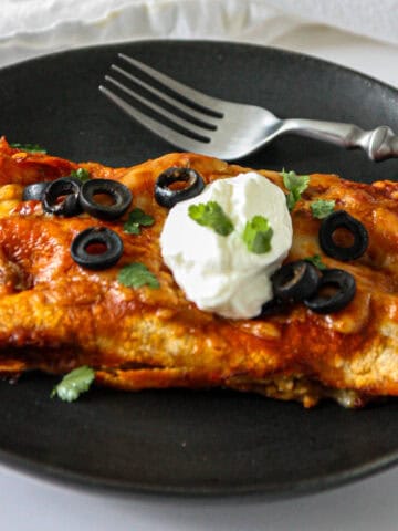 Two leftover turkey enchiladas on a black plate with a silver fork