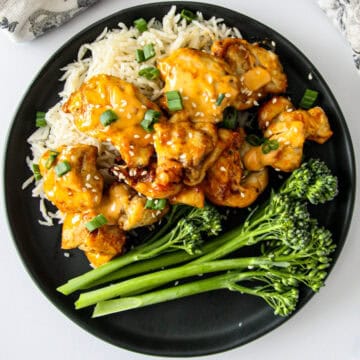 Bang bang chicken on a bed of rice on a black plate.