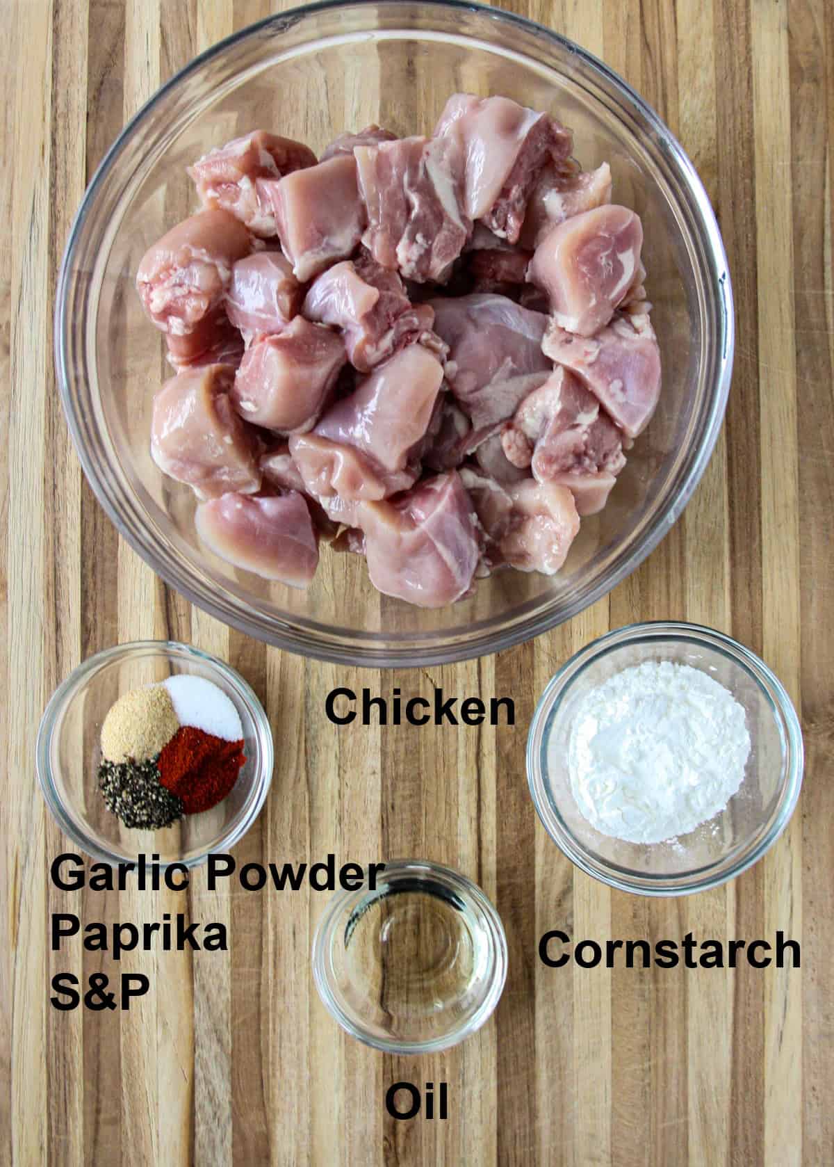 The ingredients for the baked chicken, in glass bowls on a wooden board.