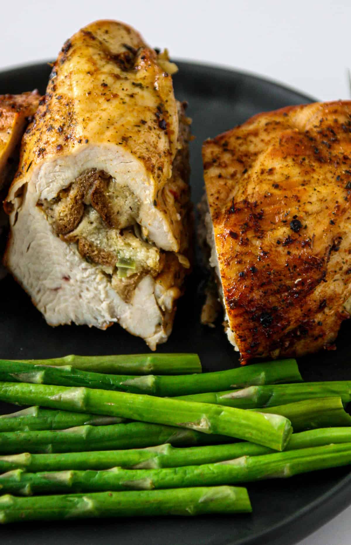 A slice of stuffed chicken breast on a black plate with asparagus.